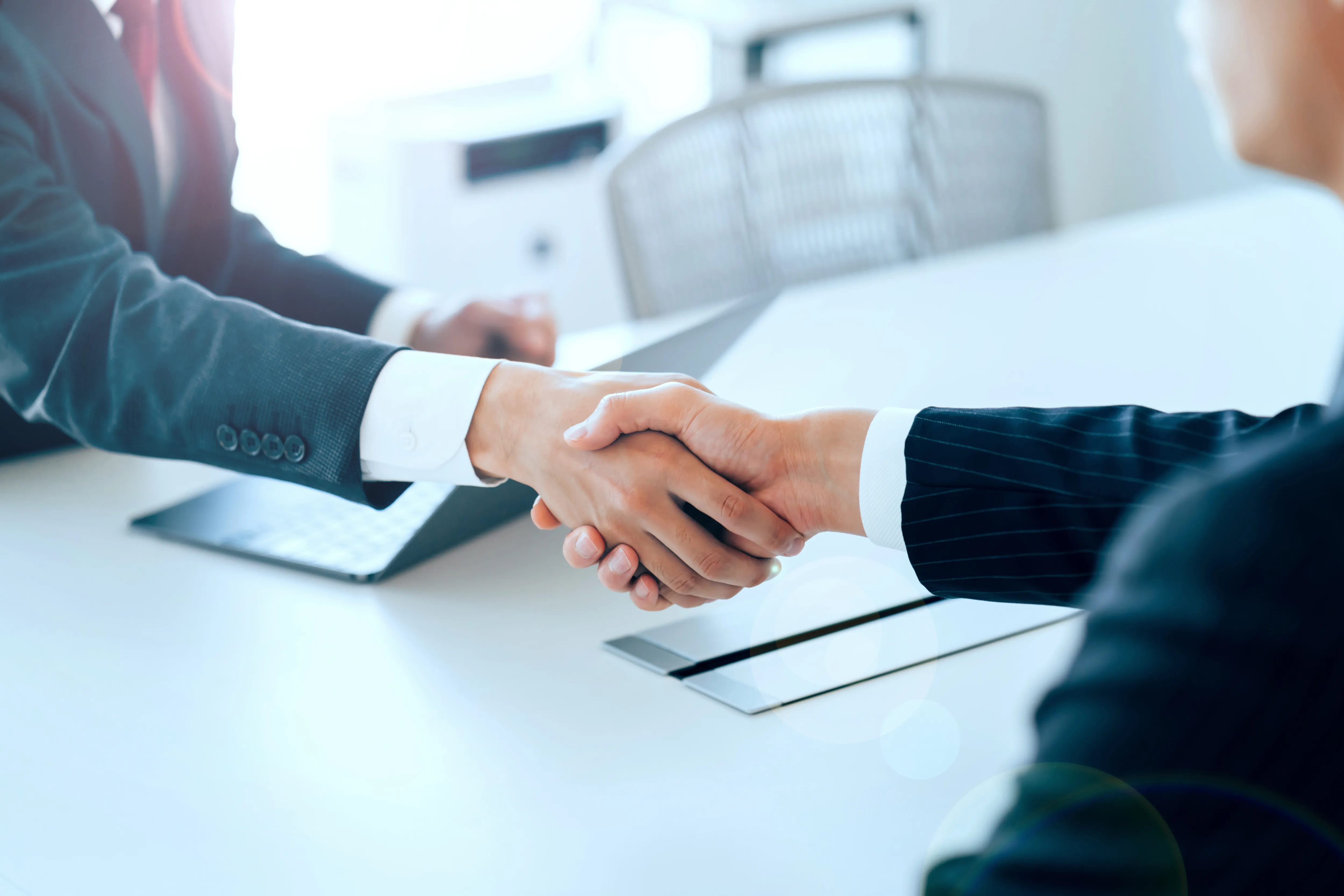ビジネススーツを着た二人がオフィスの机の上で握手している様子。
