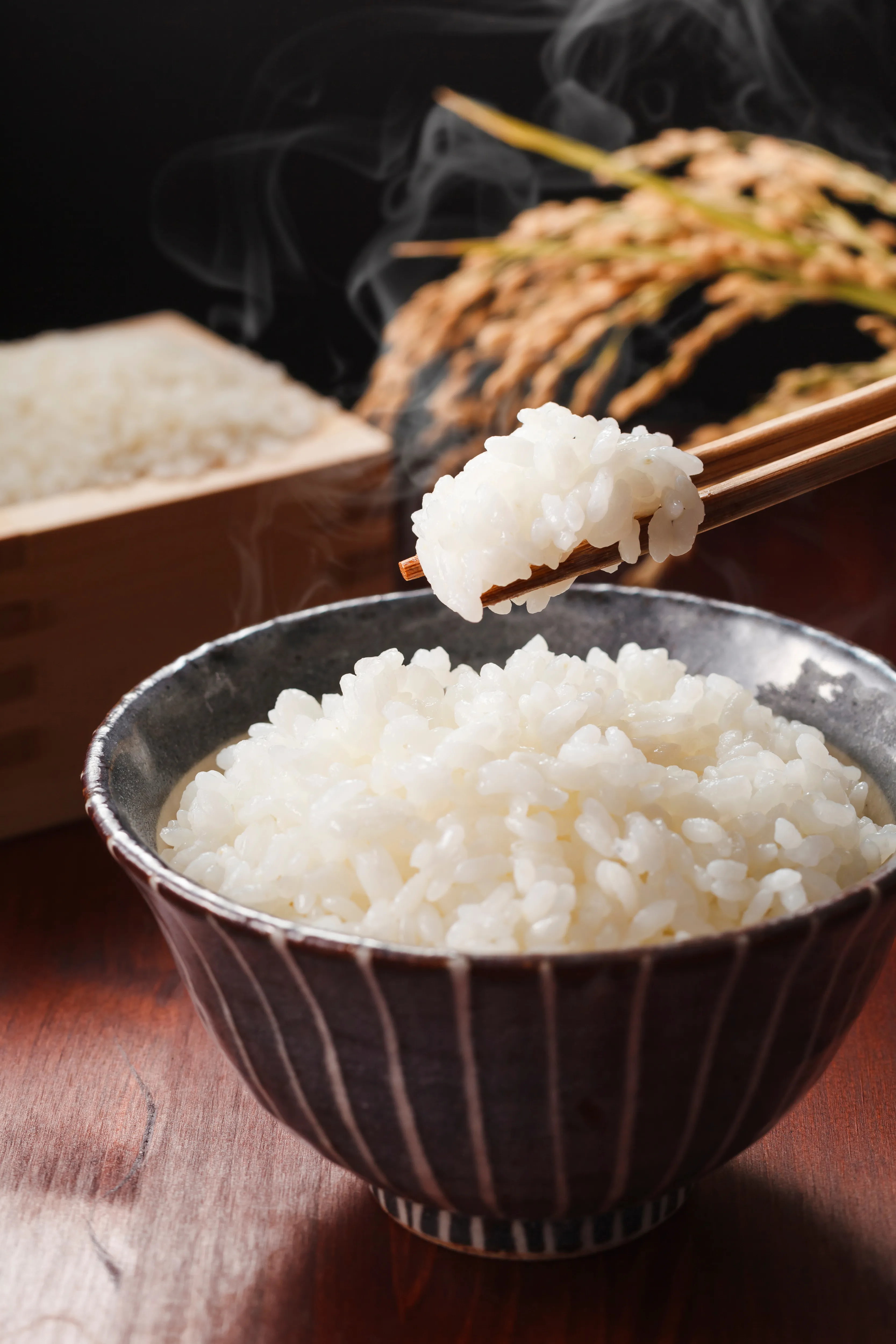 湯気の立つ茶碗に盛られた炊きたての白ご飯を箸でつまんでいる様子。