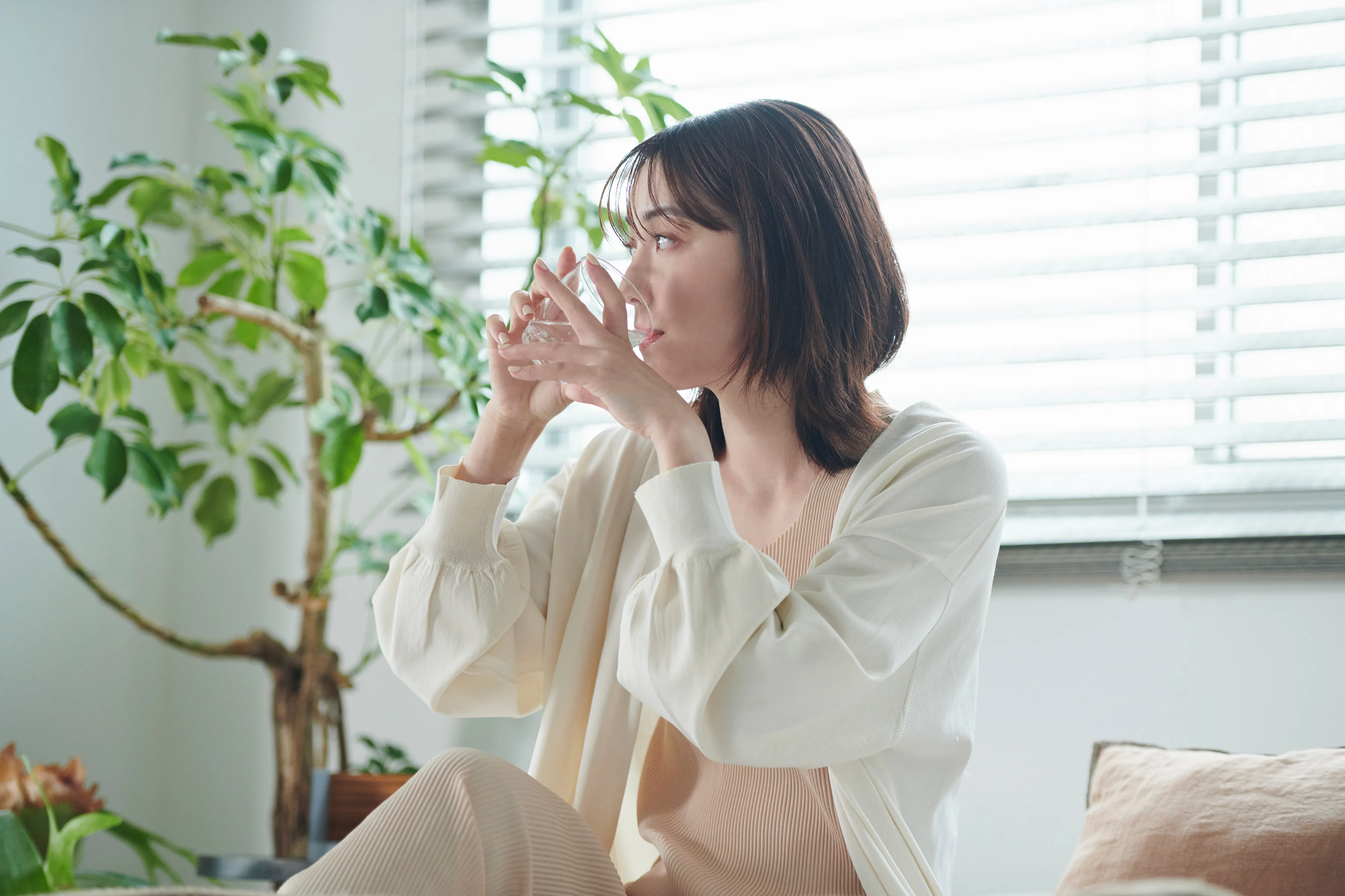 窓辺でグラスから水を飲んでいる女性。