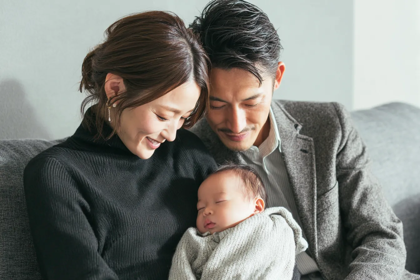 赤ちゃんを抱きながらソファに座って微笑む両親の家族写真。