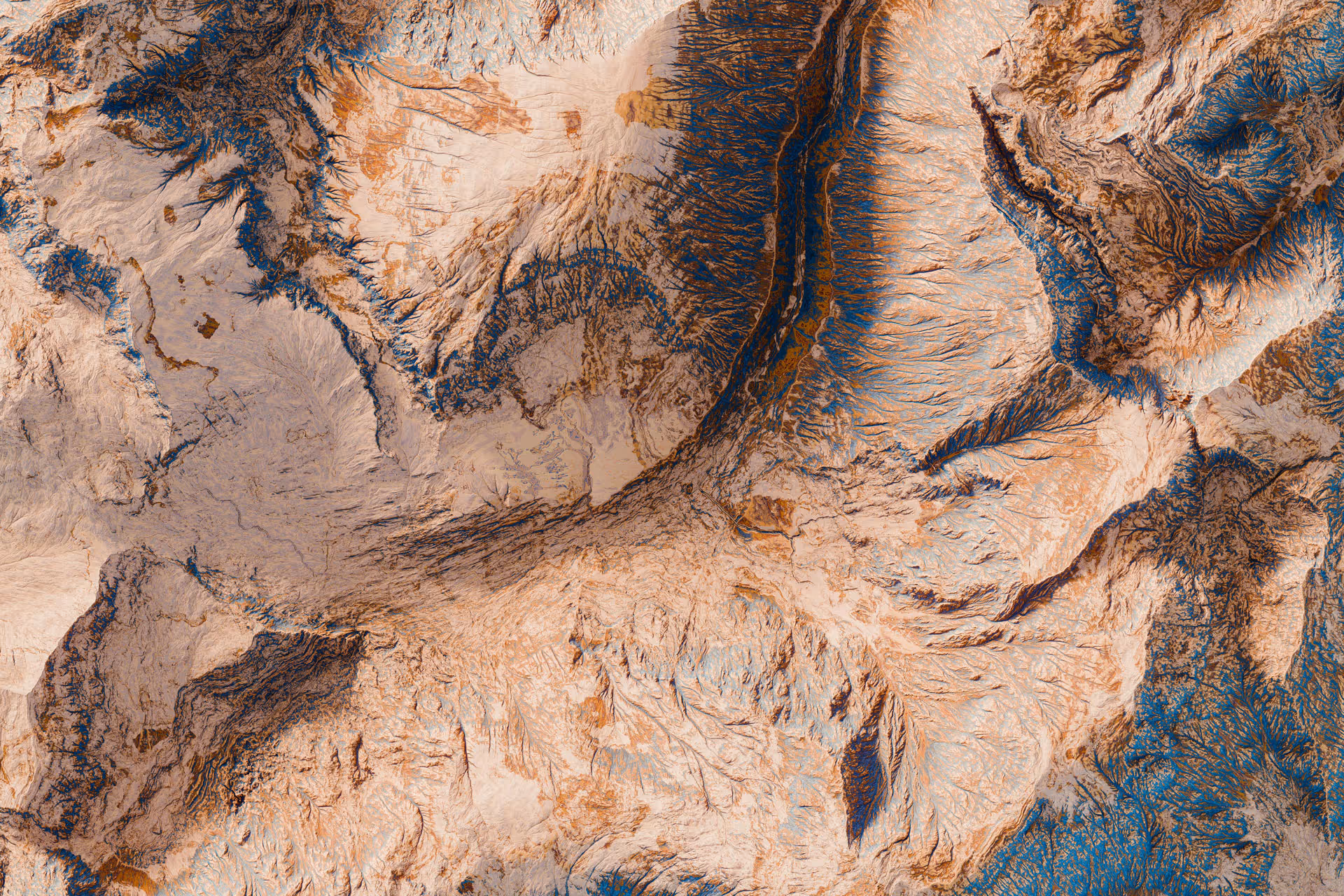 Aerial view of arid land with rugged terrain and deep canyons in earthy brown and beige tones.