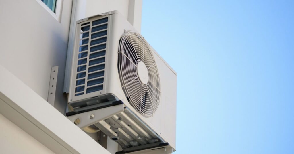 Outdoor air conditioning unit mounted on the side of a building against a clear blue sky.