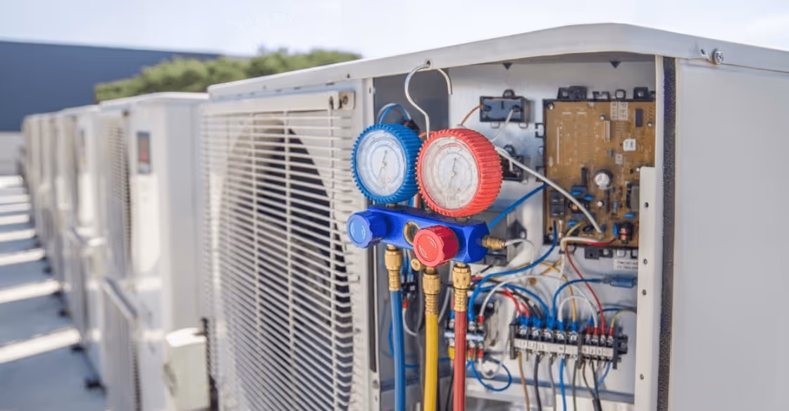 Close-up of HVAC system with pressure gauges and colored hoses attached to outdoor air conditioning units.