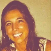 Smiling woman with long dark hair wearing hoop earrings against a plain background.