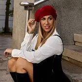 Woman wearing a red beret, white long-sleeve shirt, black dress, and knee-high boots sitting on stone steps.