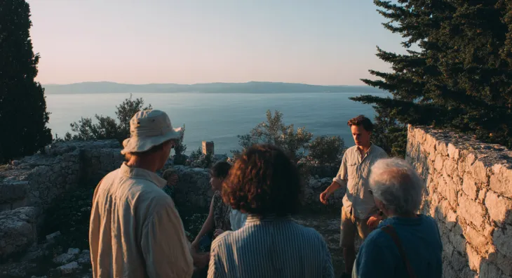 A small group of people talking near stone ruins with the ocean in the background.