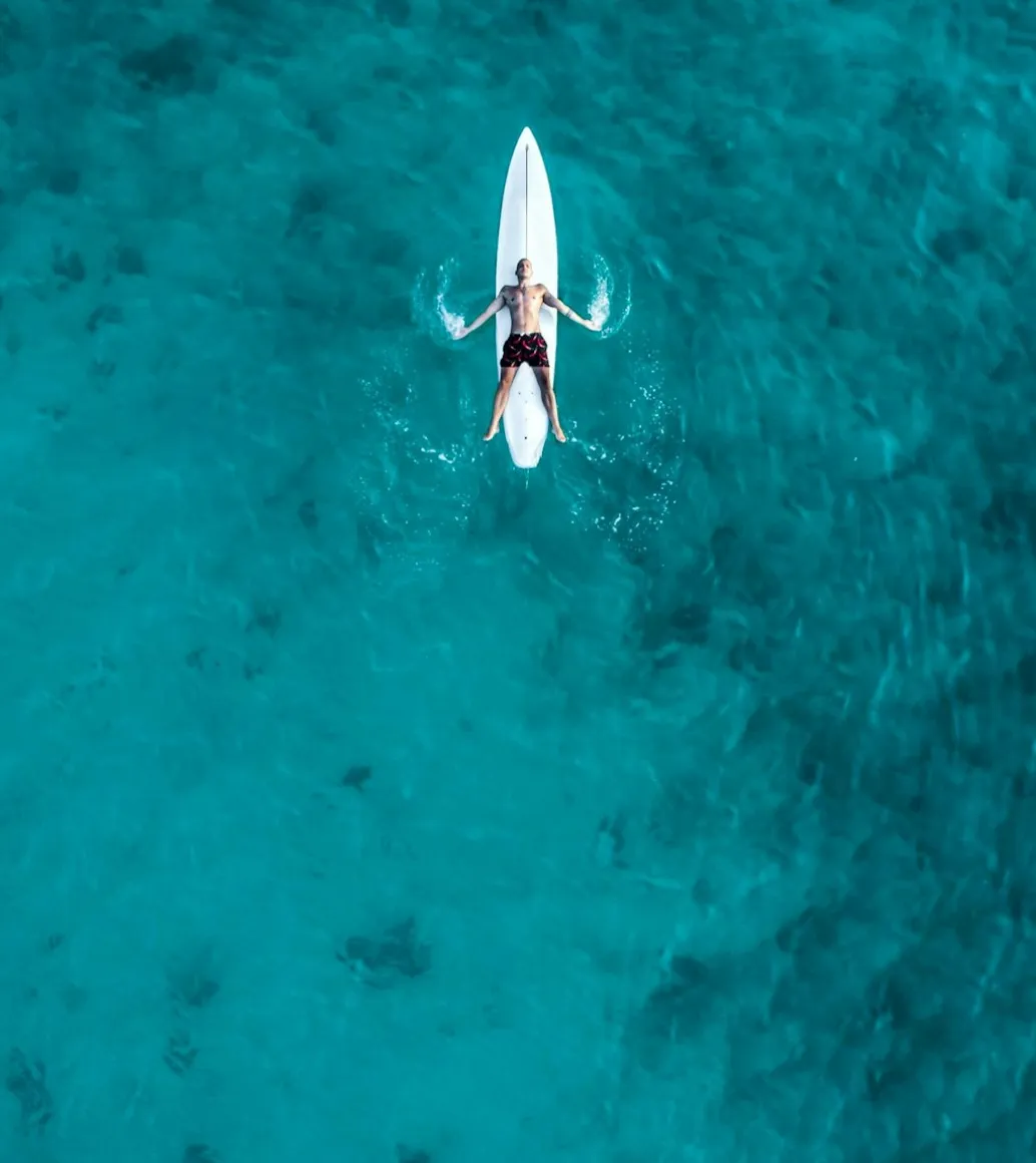 A person lying on a surfboard in clear blue water.