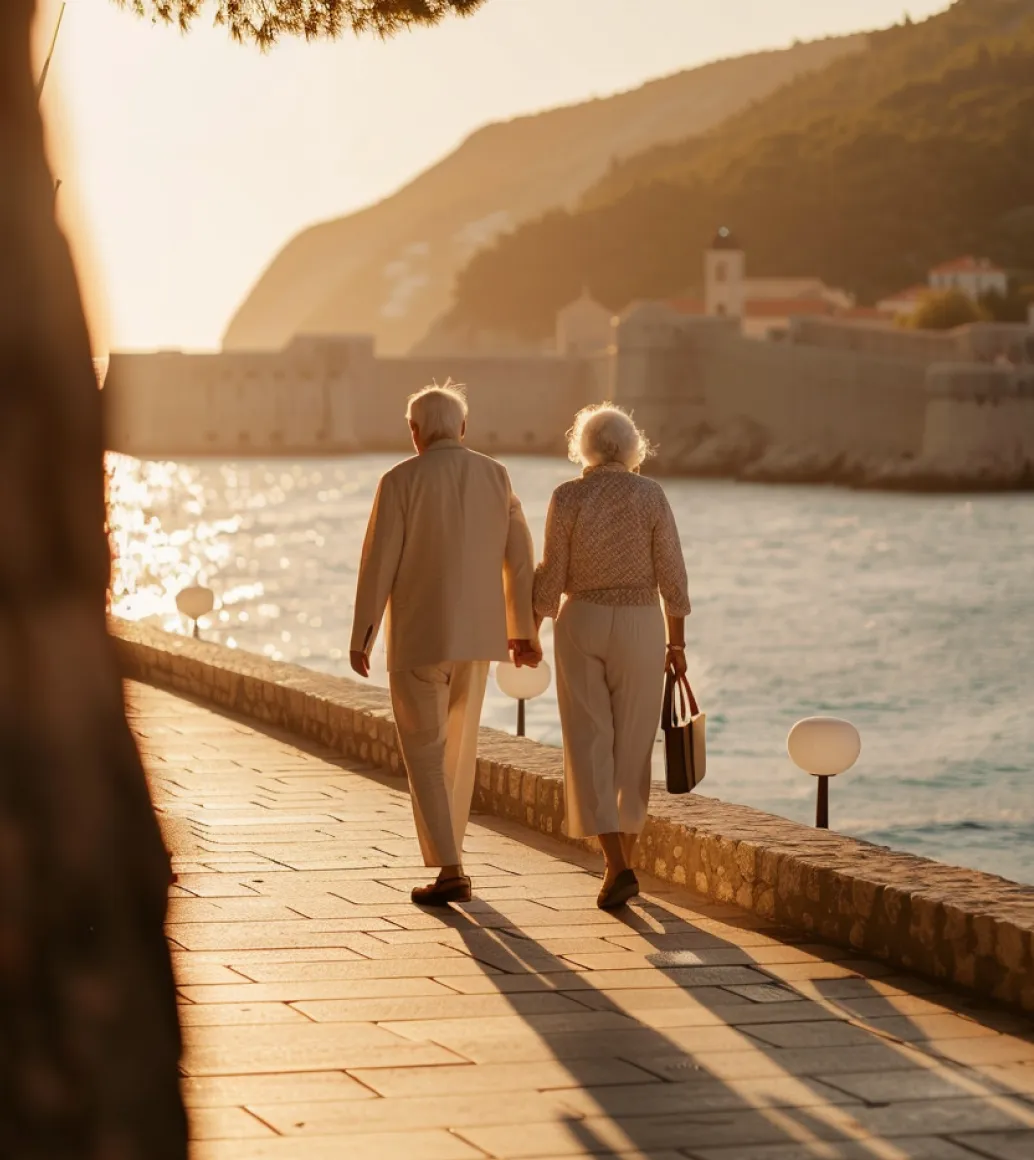 An older couple walking hand in hand along a seaside path at sunset.