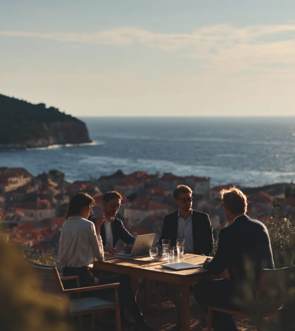 Four people having a meeting at a table overlooking the sea and rooftops.