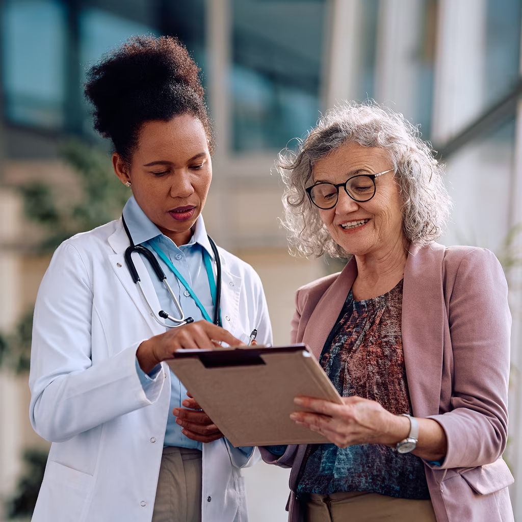 Female doctor with stethoscope discussing medical information on a clipboard with an elderly woman.