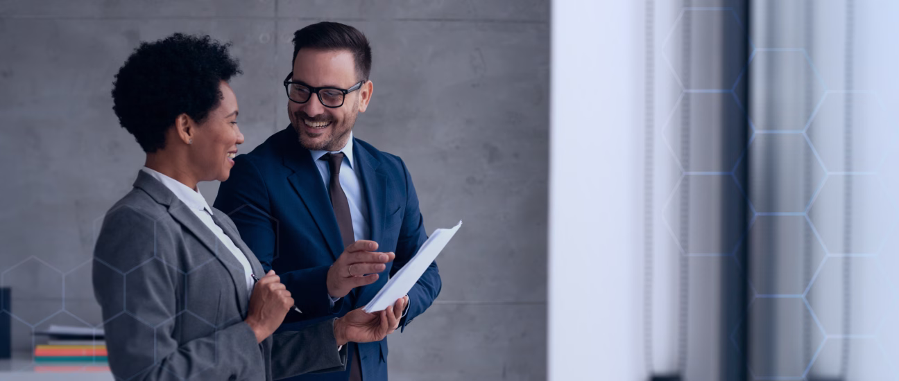 Two business professionals, a man and a woman, smiling and discussing documents in an office setting.