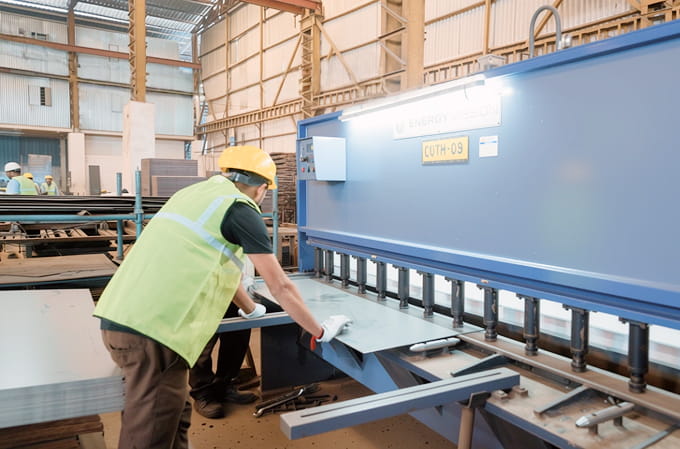Worker in safety gear operating a large blue industrial metal cutting machine inside a factory.