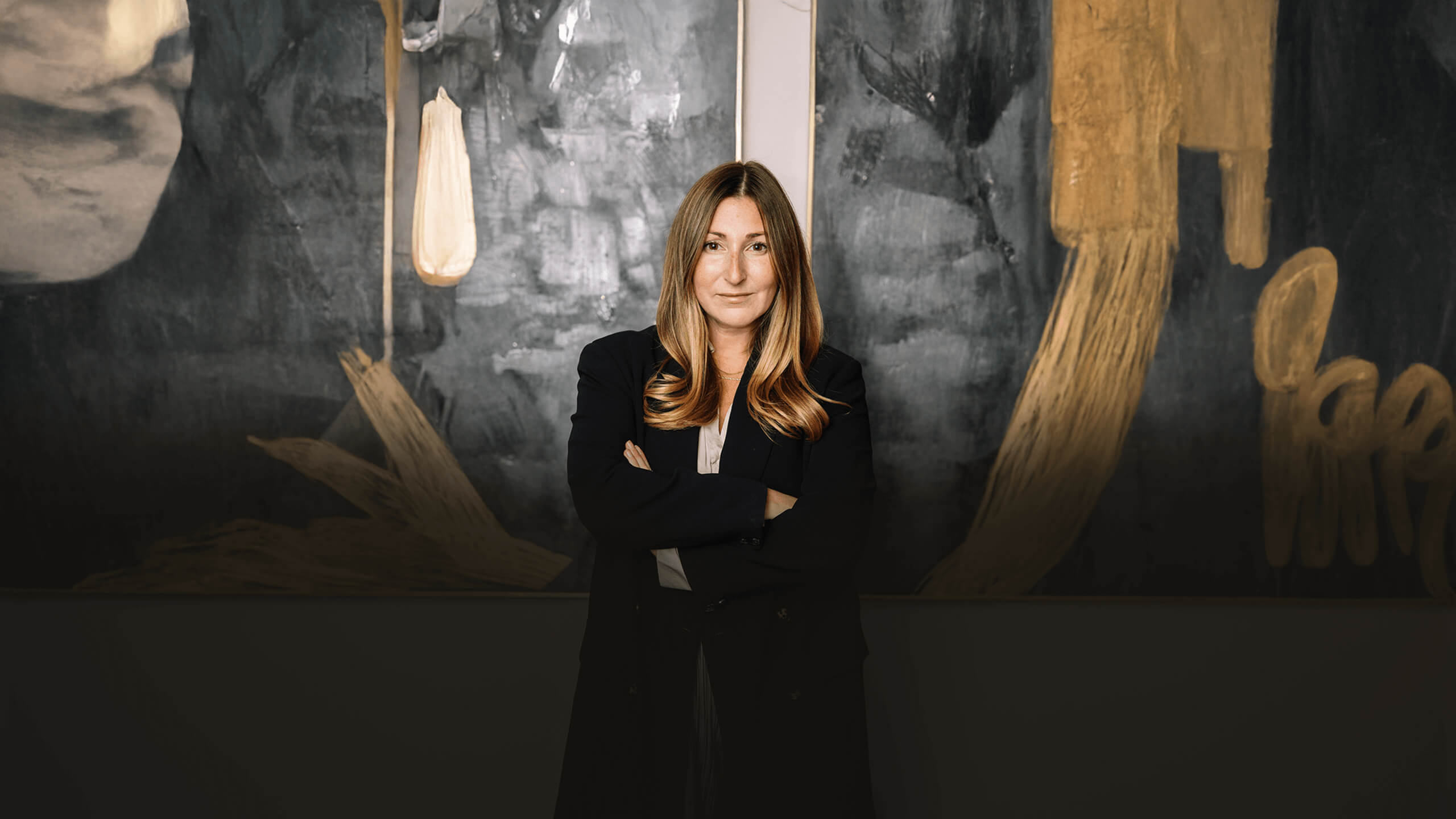 Samantha Eisen stands with arms crossed against a dark abstract art background.