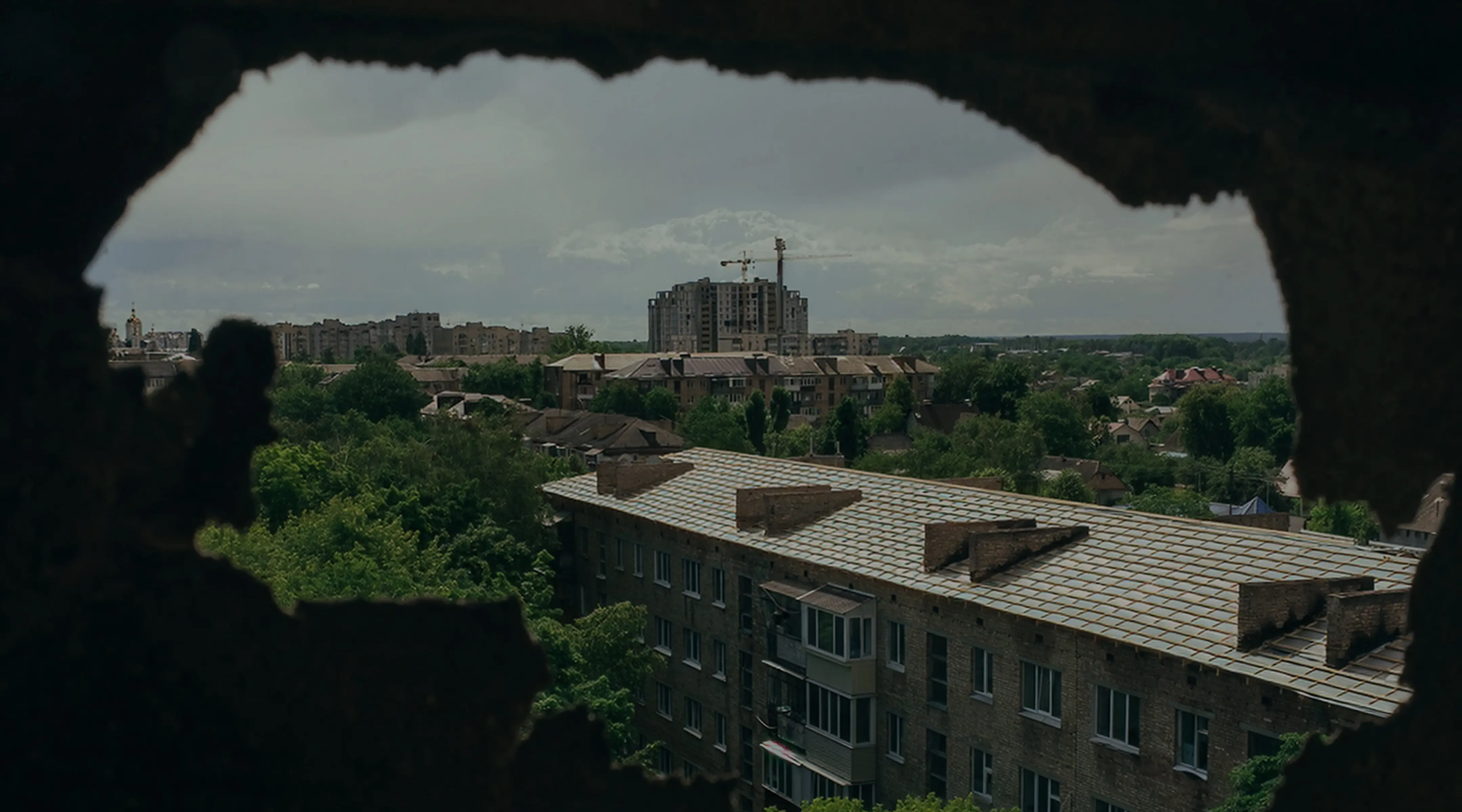 View of residential buildings and greenery through a hole in a dark wall.