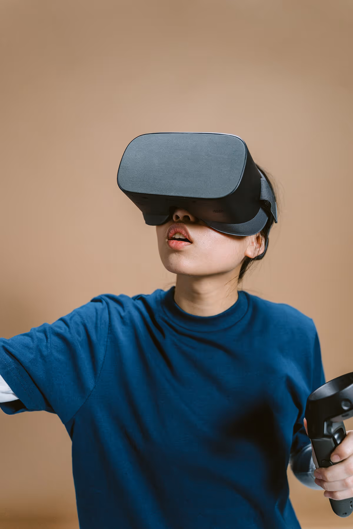 Person wearing a virtual reality headset and holding a VR controller against a plain beige background.