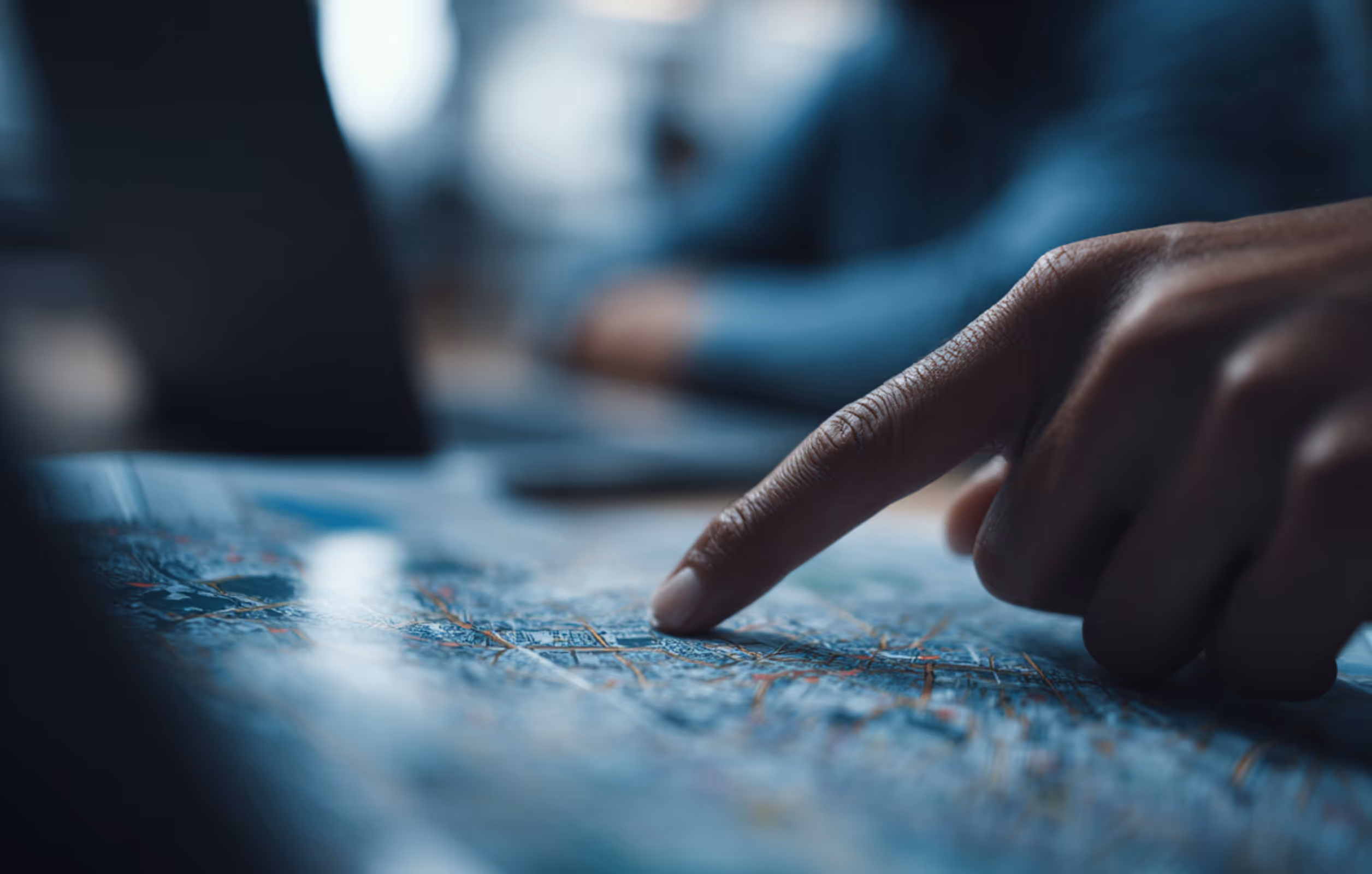 Close-up of a hand pointing at a detailed map on a table in a dimly lit room.
