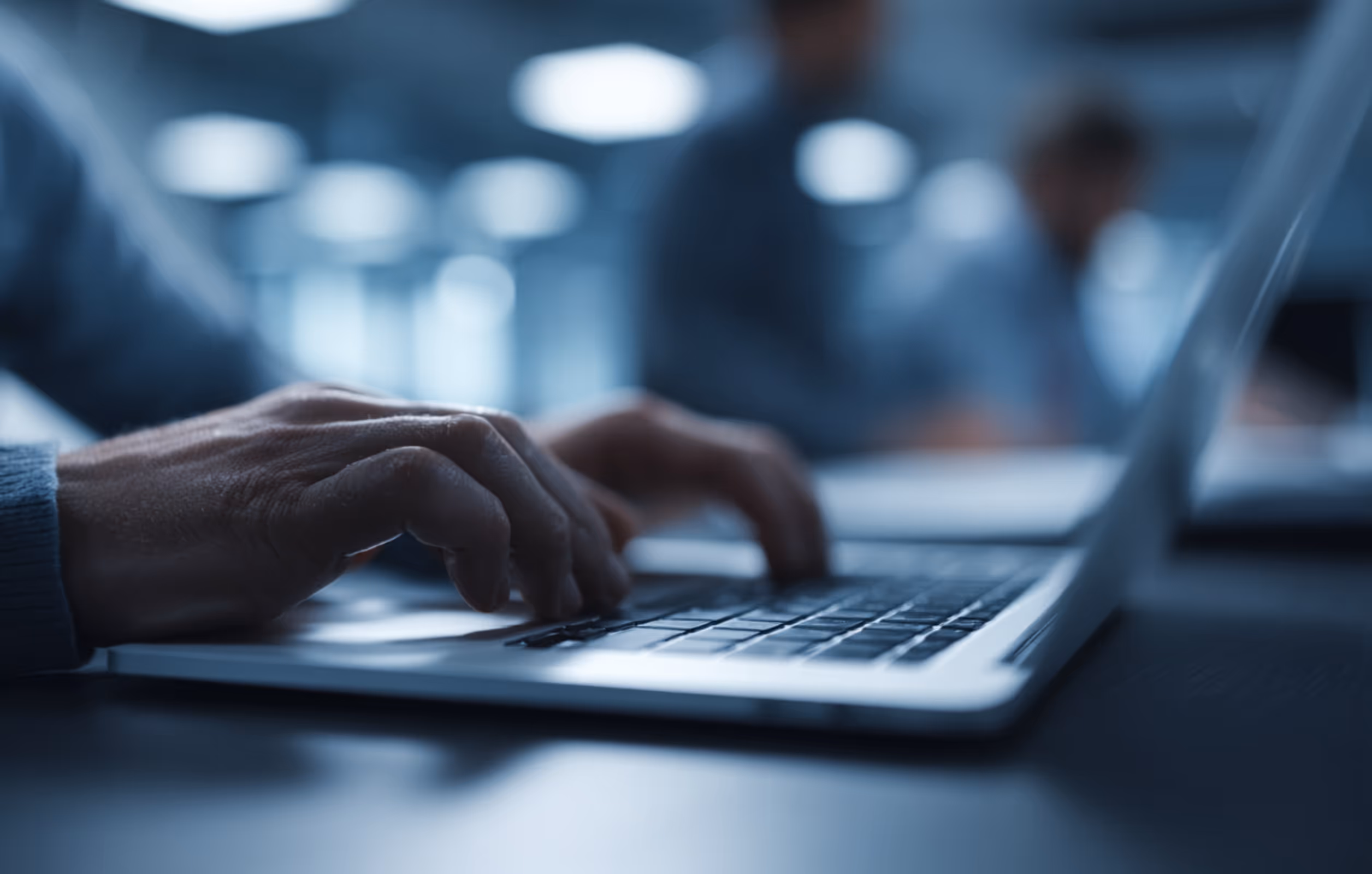 Close-up of hands typing on a laptop keyboard in a dimly lit office.