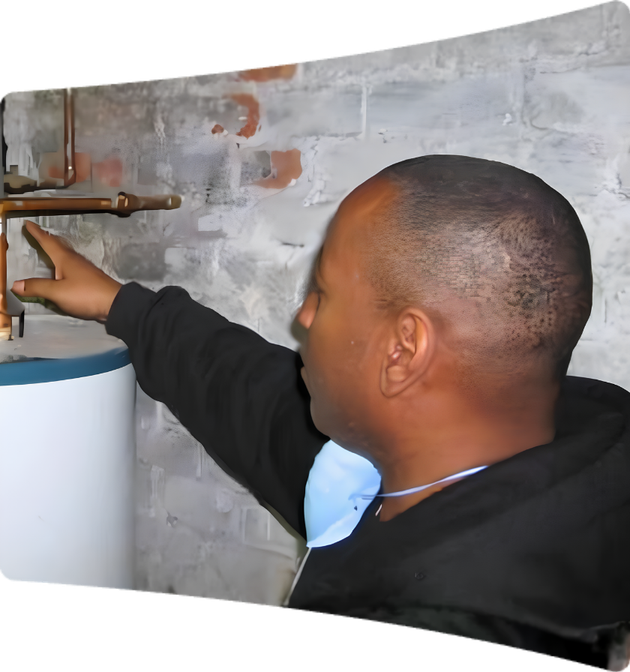 Person pointing to a valve on a water heater tank near a brick wall during a MassIPL Environmental Stewardship Assessment.