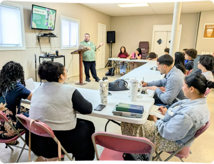 Man stands at podium giving presentation to seated group in a meeting room.