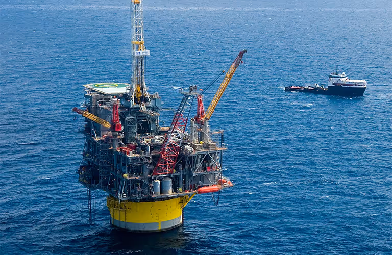 Offshore oil rig platform with cranes in the ocean and a supply boat nearby.