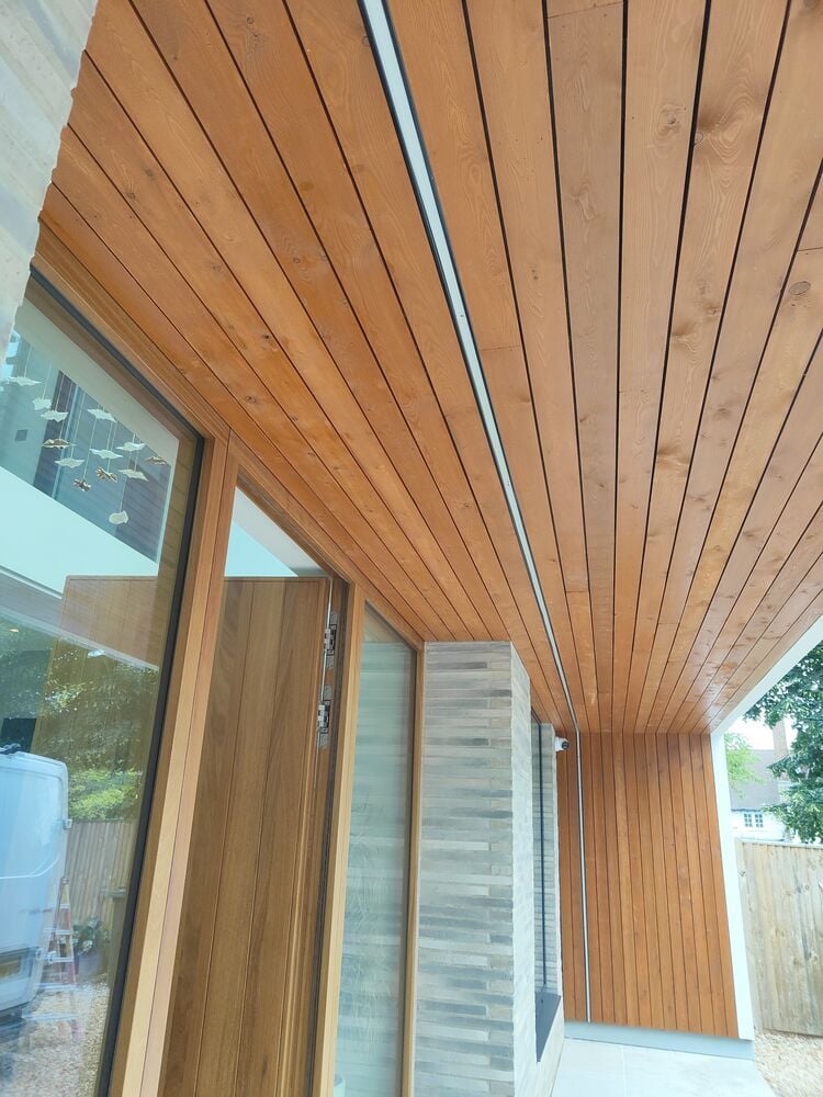 Modern wooden ceiling and wall paneling on a covered patio area with glass doors and a light gray tiled floor.