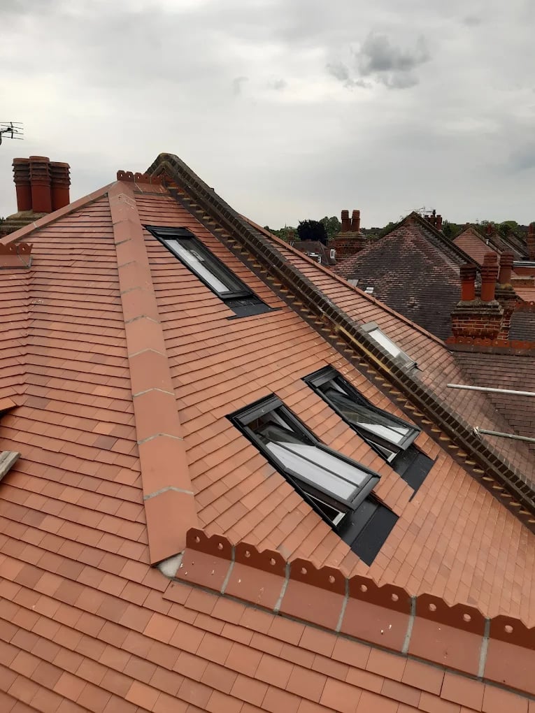 Sloped red tile roof with three skylights and multiple chimneys under an overcast sky.