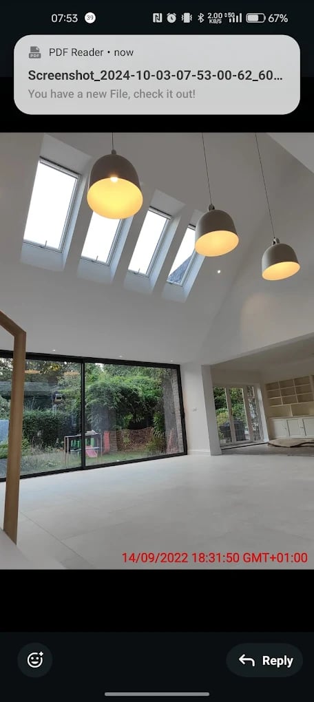 Modern interior room with large floor-to-ceiling sliding glass doors, three hanging pendant lights, and skylights on a slanted ceiling overlooking a green garden.