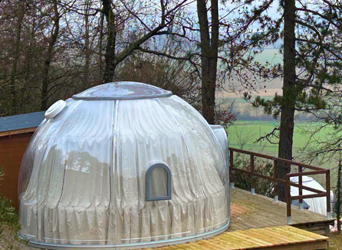 Dôme transparent installé sur une terrasse en bois avec des arbres en arrière-plan.