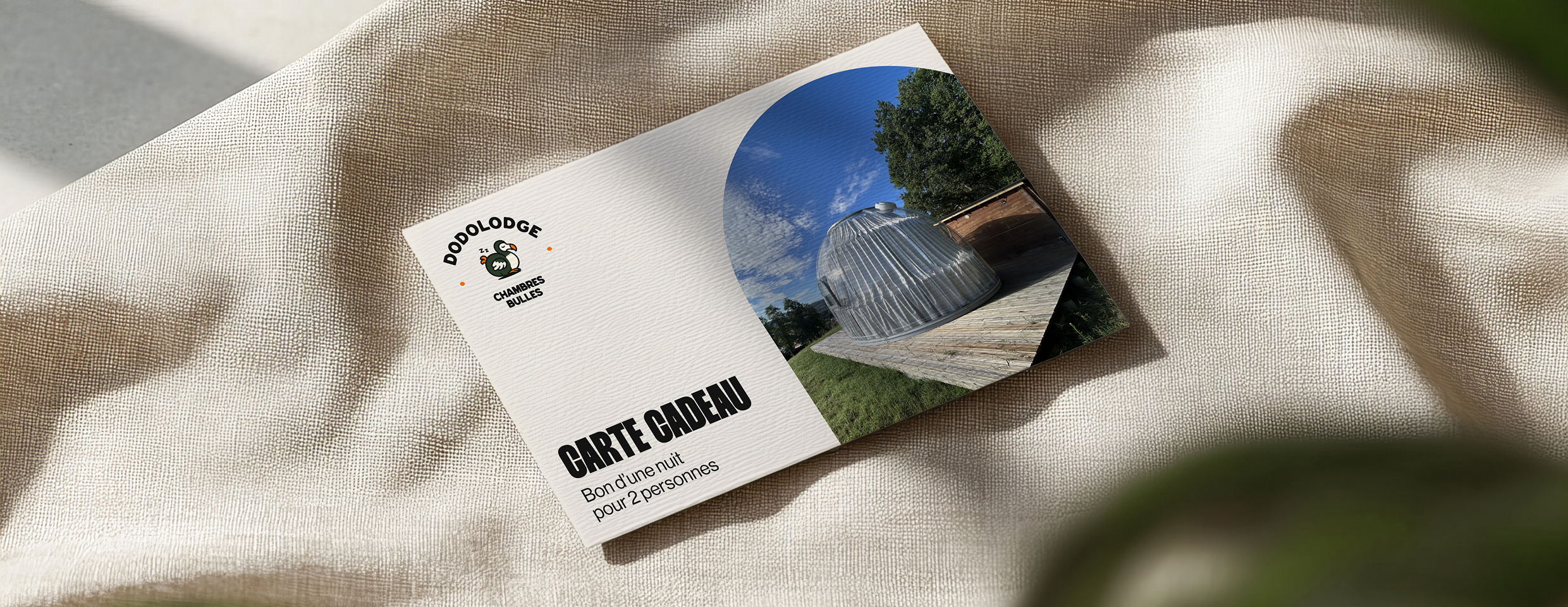 Carte cadeau Dodolodge avec photo d'une chambre bulle transparente sur une terrasse en bois dans un environnement naturel.