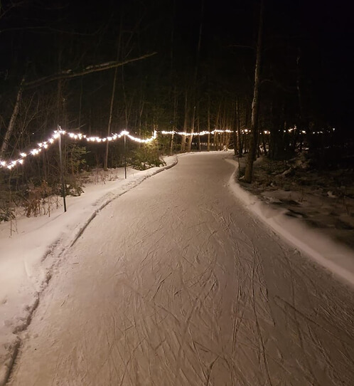 A skating trail at night, lined with christmas lights to see. There are a lot of skate prints on the ice.