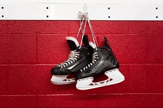 Pair of hockey skates hung on a hook in the dressing room. The wall colour is a bright red