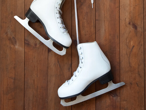 Pair of figure skates hanging on a hook. The wall in a wooden