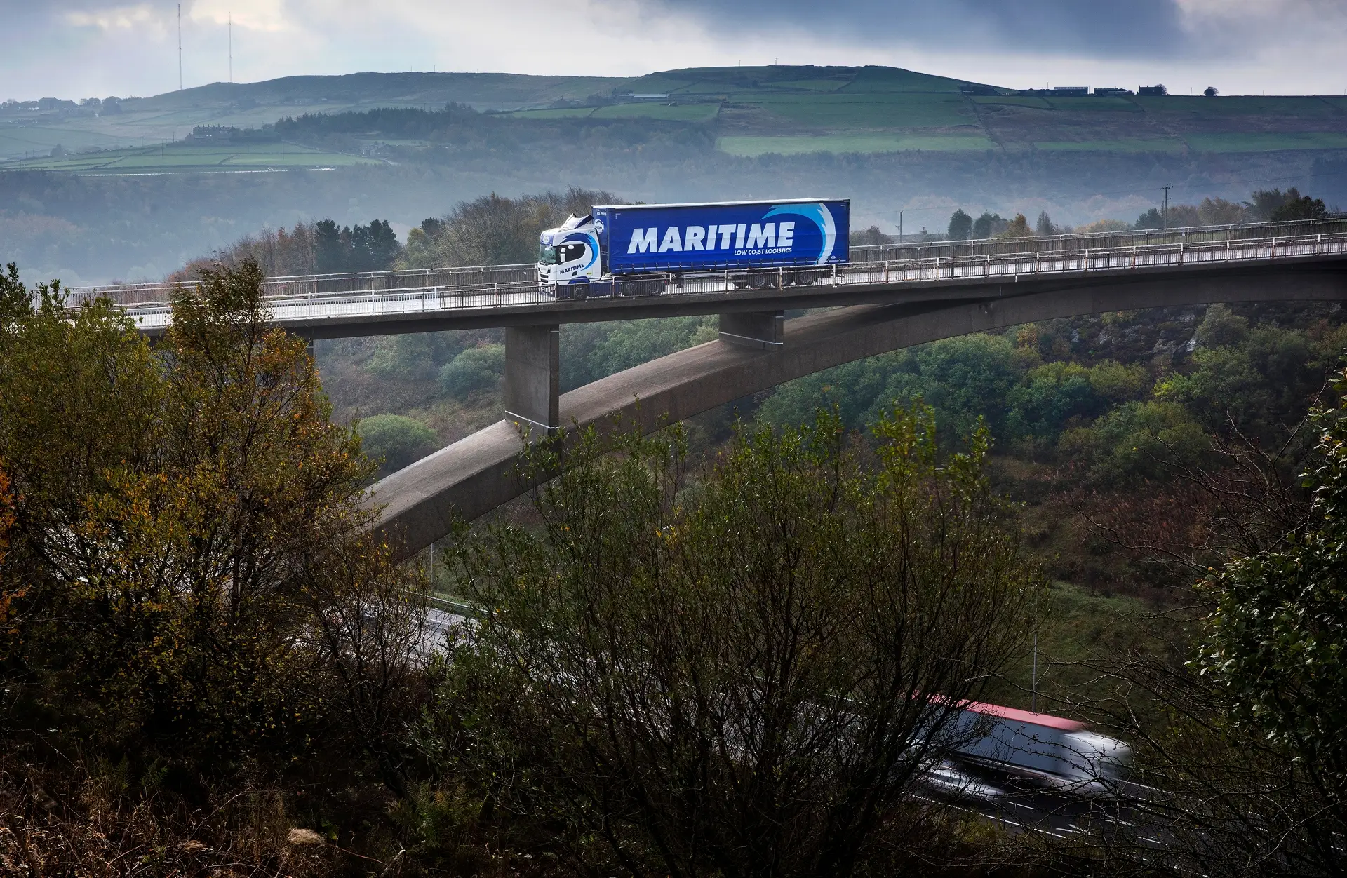 Maritime Transport curtainsider HGV on a bridge surrounded by greenery