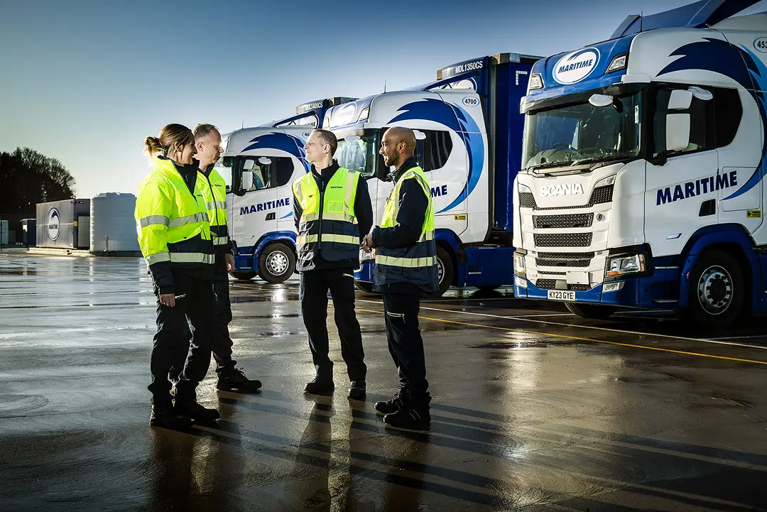 Four drivers in high-visibility clothing having a discussion in a vehicle yard