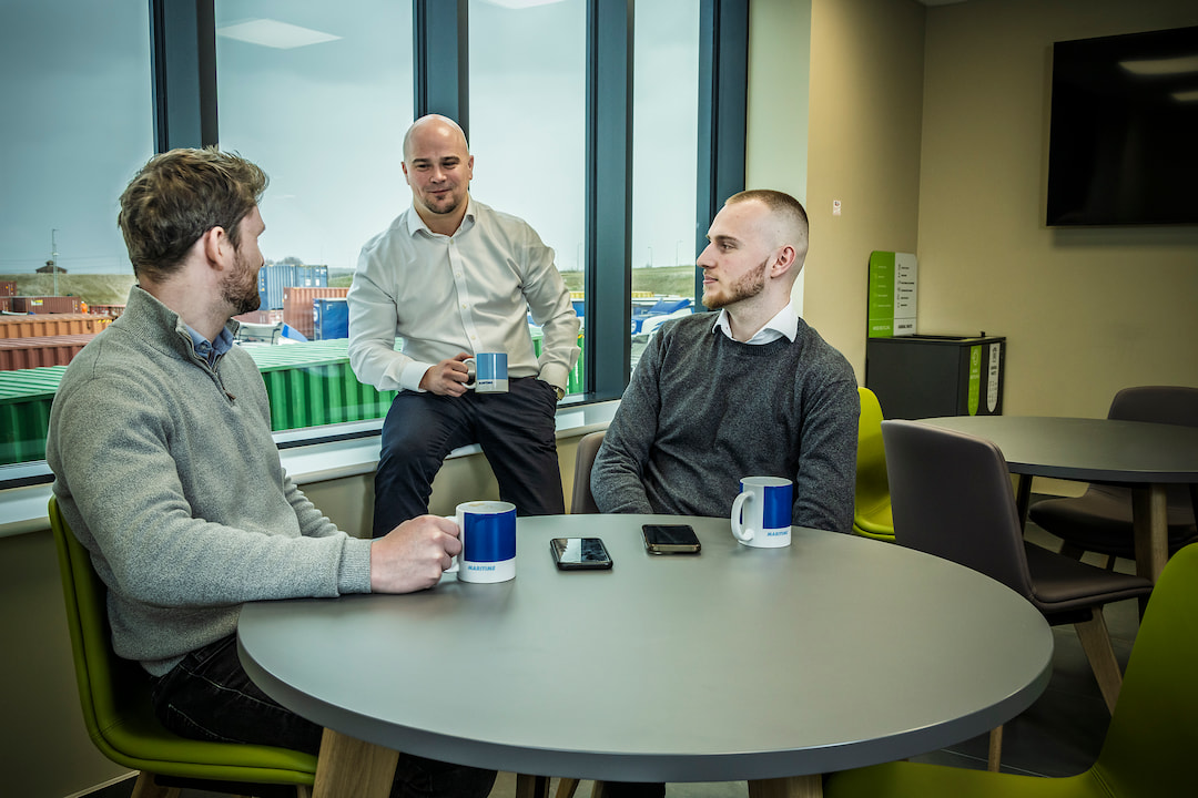 Three office workers having a conversation in a Maritime Transport breakroom.