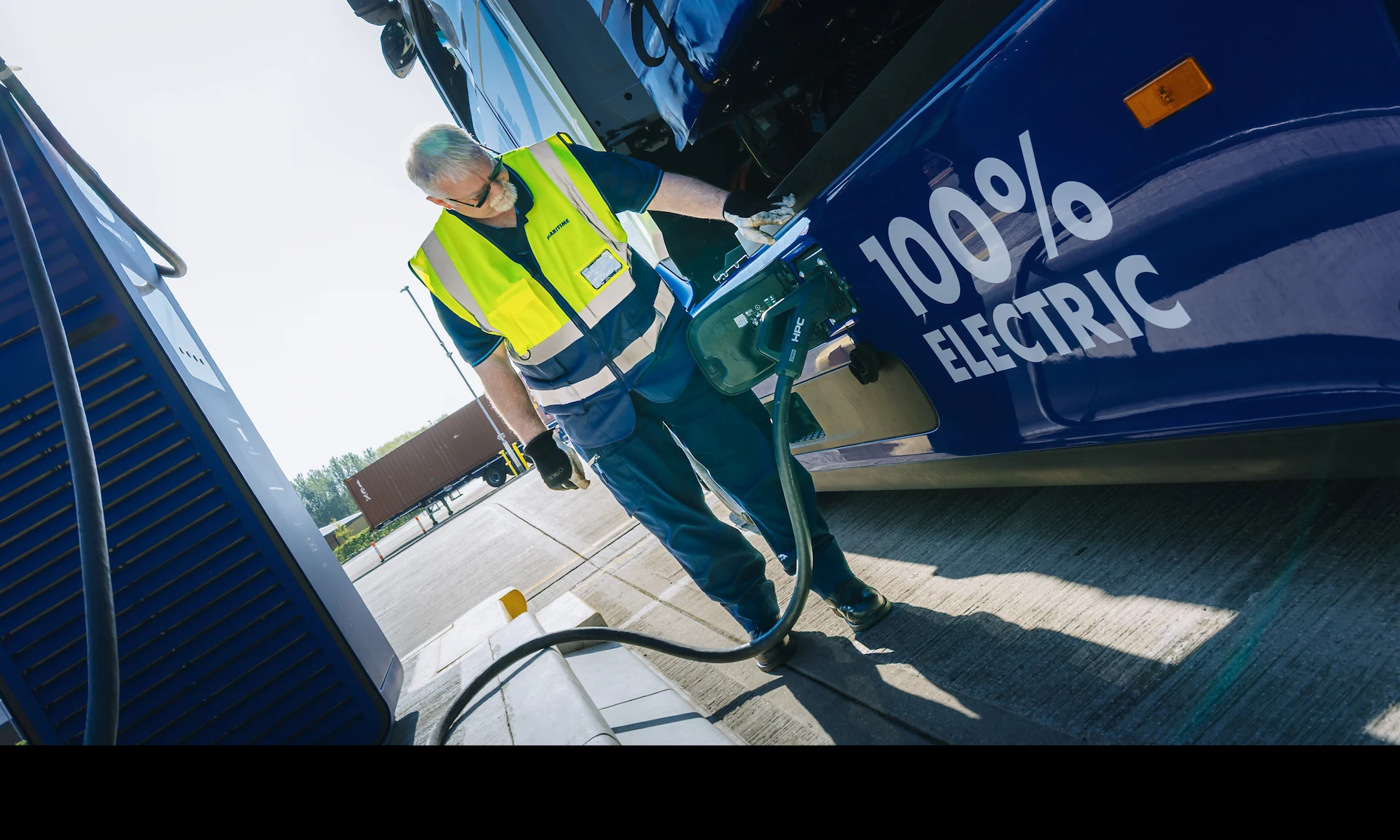 A Driver in high-visibility clothing charges an electric HGV.