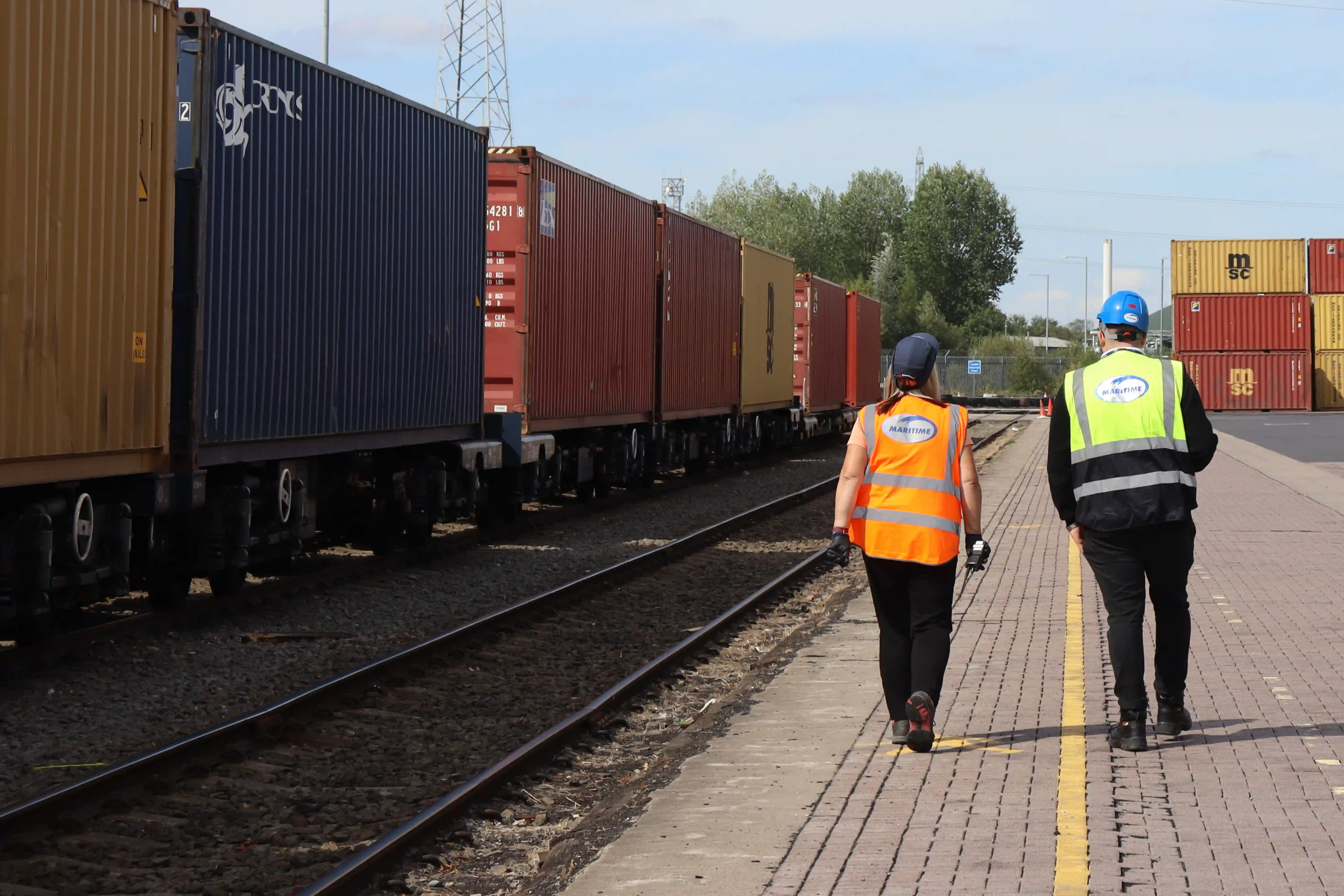 Two people in high-visibility vests walk next to train.