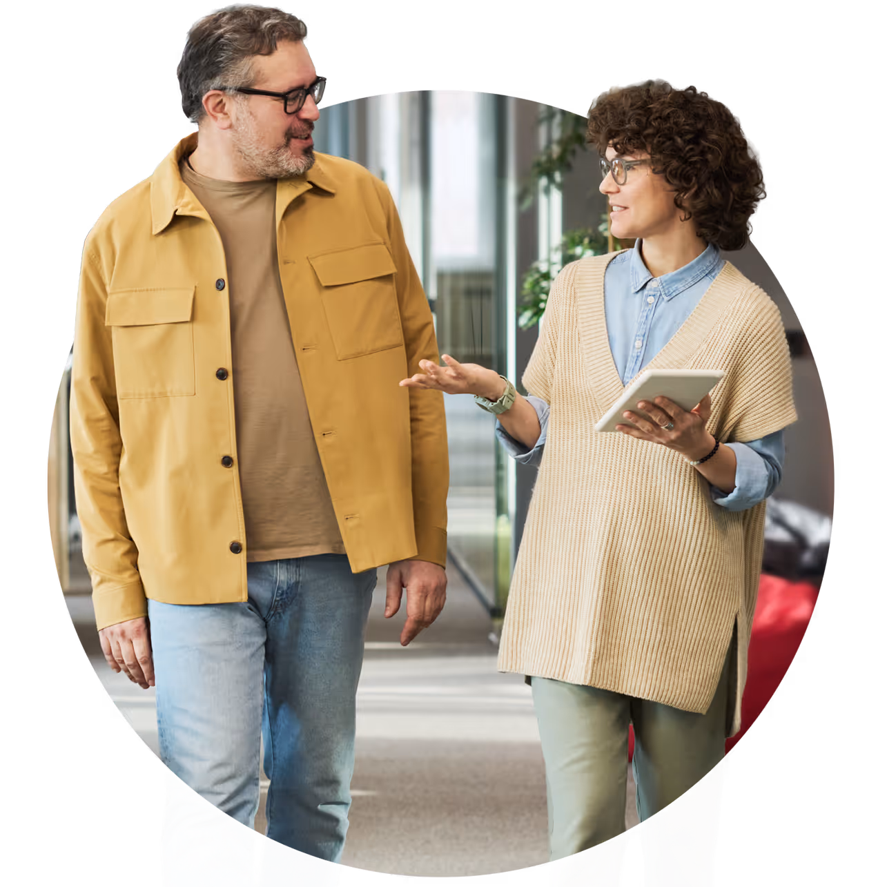 Two colleagues walking and talking in an office, one holding a tablet.