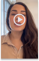 Young woman with long dark hair speaking indoors near a window, wearing a beige shirt.