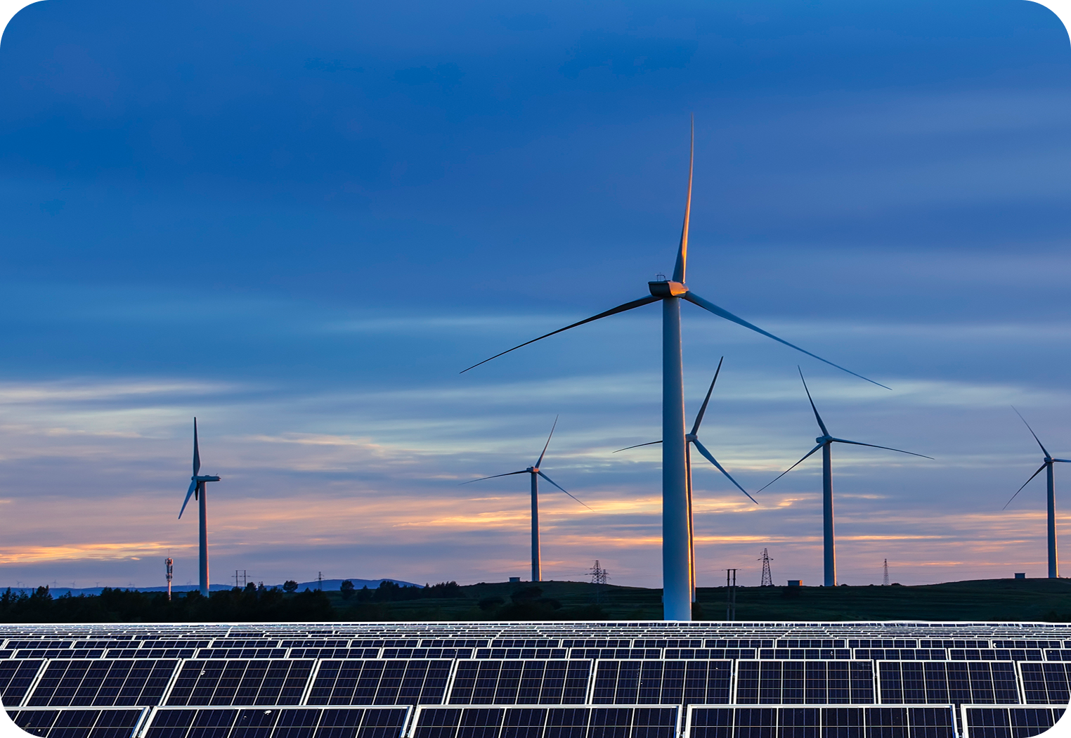 Rows of solar panels in front of wind turbines under a blue sunset sky.