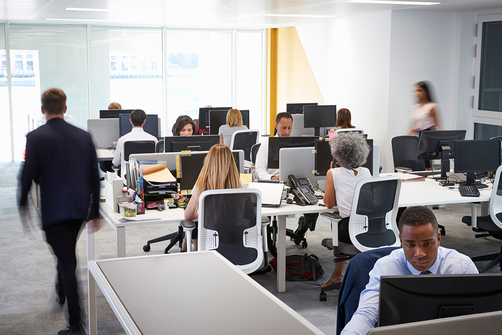 Busy modern office with diverse employees working at desks with computers and phones.