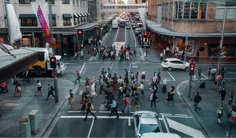 Crowded urban crosswalk with pedestrians crossing on a busy city street with traffic lights and vehicles.