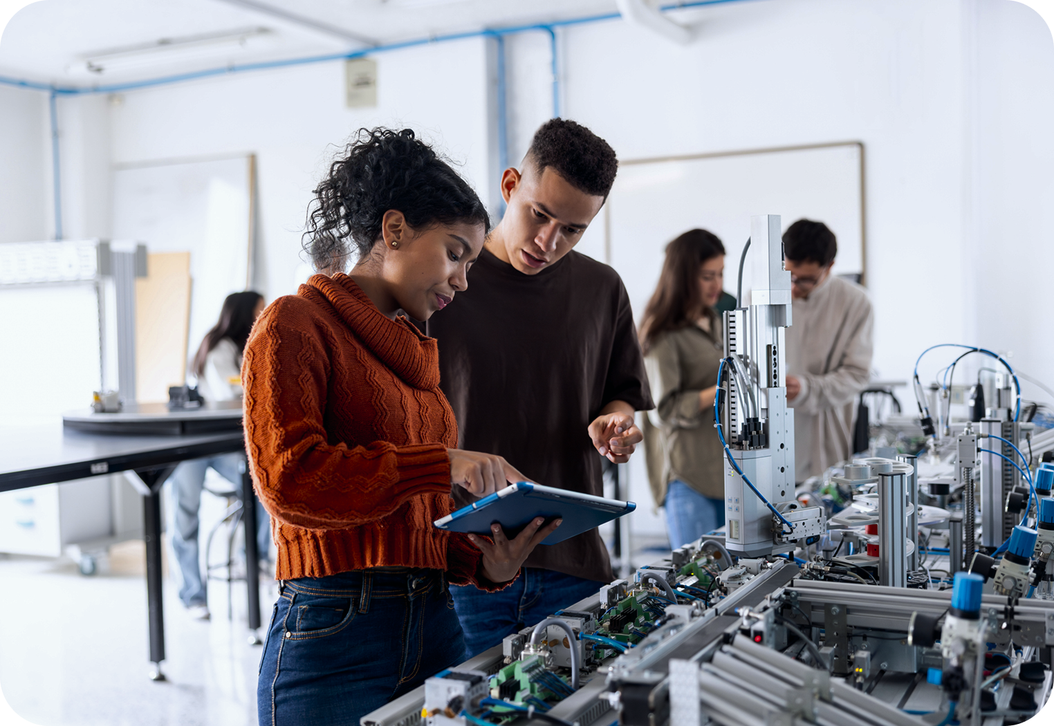 Two students studying automation machinery, one pointing at a tablet, in a modern lab setting.