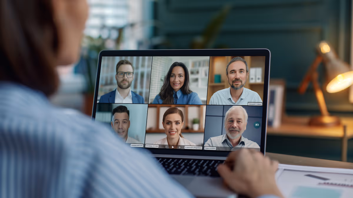 Person attending a video conference call on a laptop with six diverse participants smiling on screen.