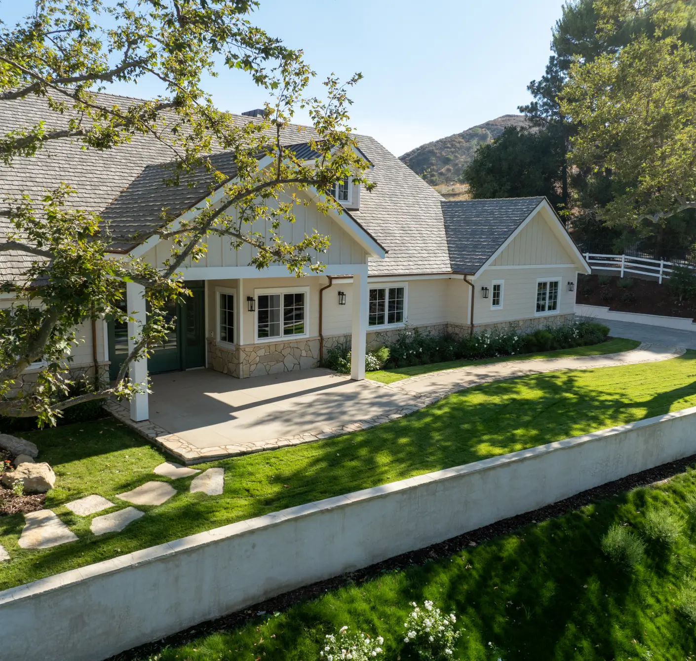 Light beige single-story house with a shingled roof, covered front porch, and landscaped green lawn with stone pathway.