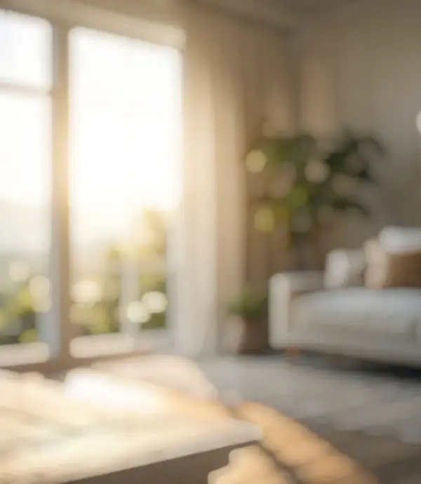 Blurred interior of a bright living room with sunlight streaming through large windows and a sofa with cushions.