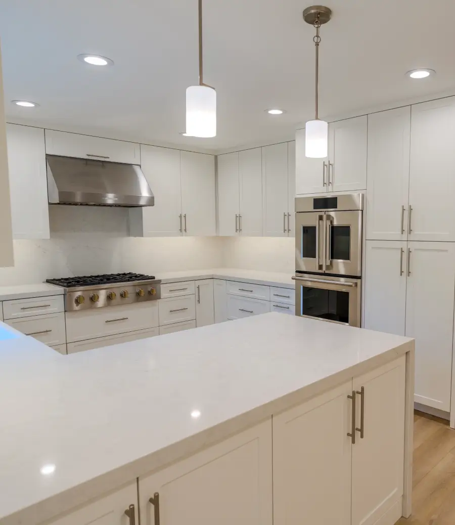 Modern kitchen with white cabinets, large island countertop, stainless steel stove, double oven, and pendant lights.