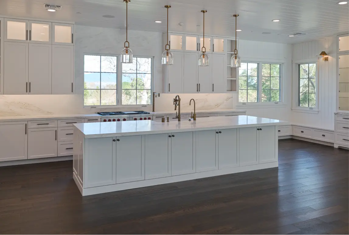 Bright modern kitchen with white cabinets, a large white island, three pendant lights, and dark hardwood floors.