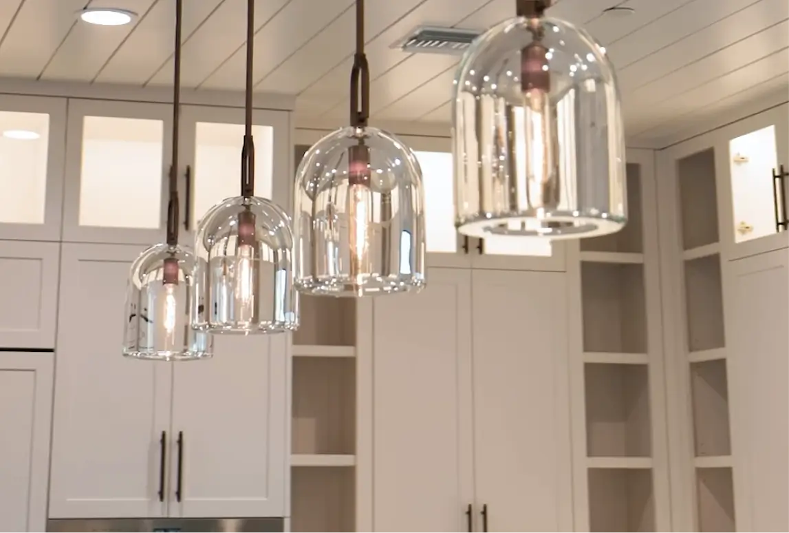Four modern glass pendant lights hanging in a kitchen with beige cabinets and a white ceiling.
