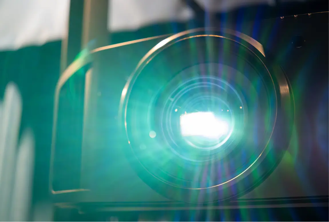 Close-up of a projector lens emitting bright light with visible lens flare.